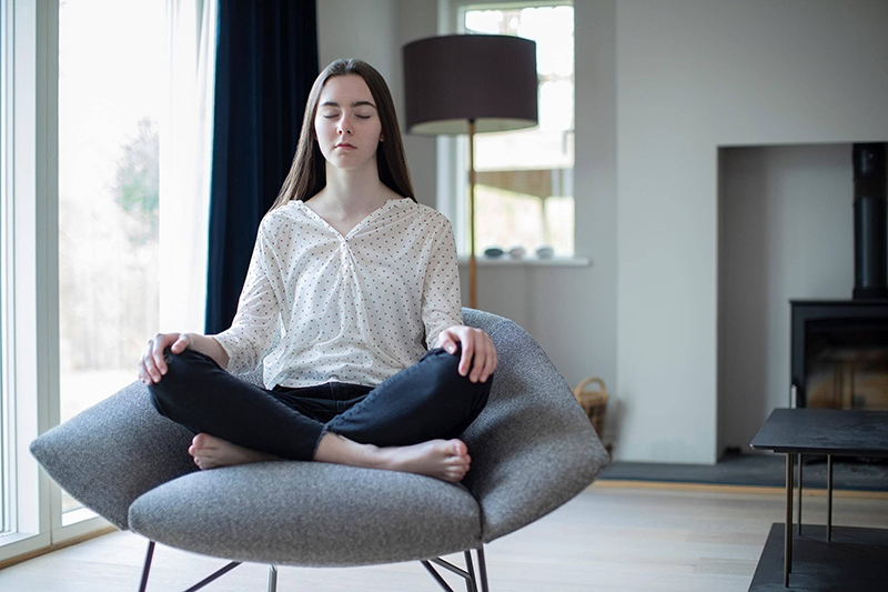 Young woman sits crossed leg in a chair while meditating Young woman sits crossed leg in a chair while meditating
