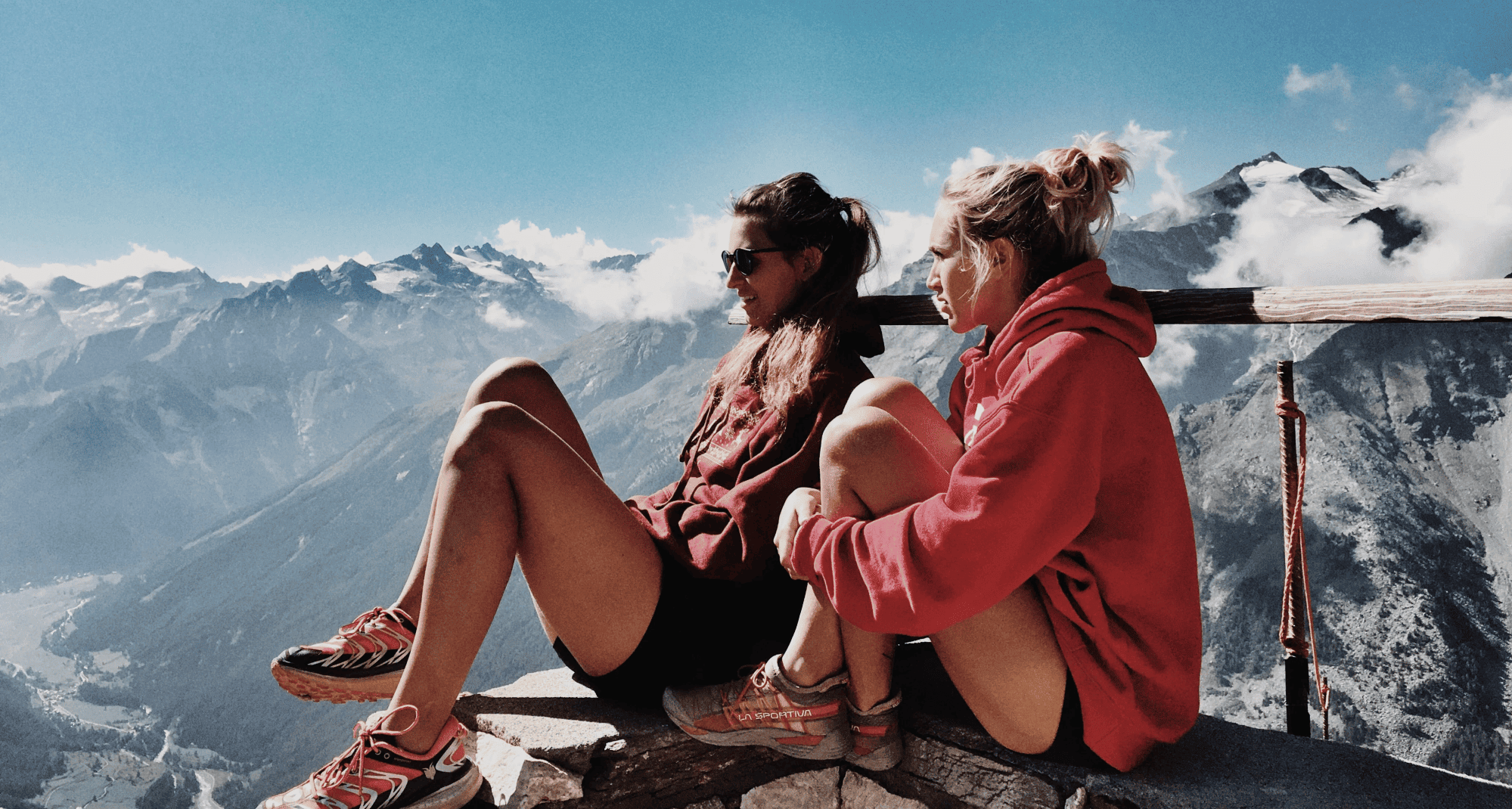 Two women sit on the edge of a mountain summit, and look out over the view. Two women sit on the edge of a mountain summit, and look out over the view.